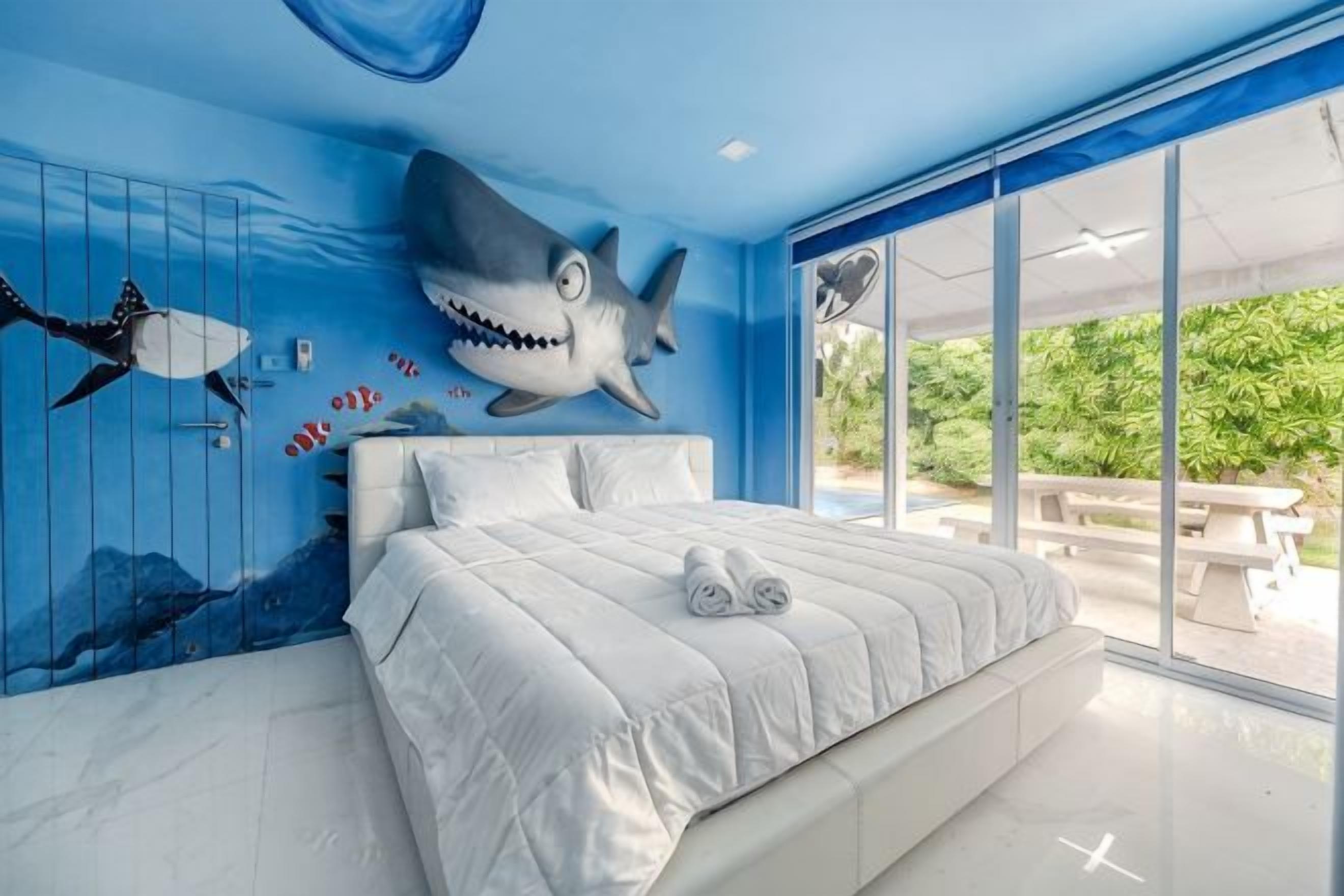 Une chambre avec un grand lit, une fresque murale représentant des requins et une vue sur l’extérieur.