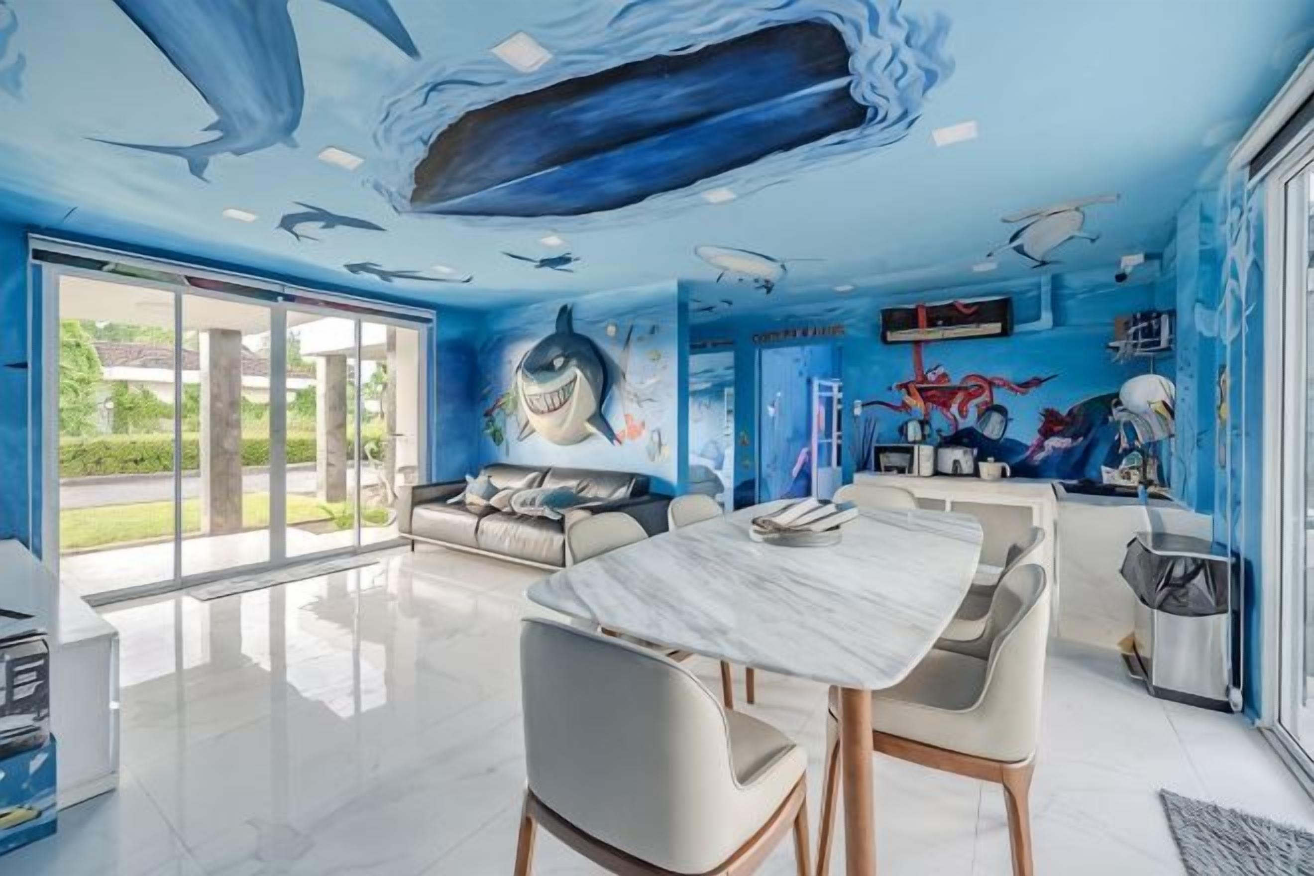 Une pièce dotée d’une grande fenêtre, d’un canapé, d’une table à manger et d’une fresque représentant des requins sur le mur.