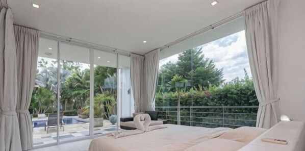 A modern bedroom with a large bed, a view of a swimming pool, and a balcony with a railing.