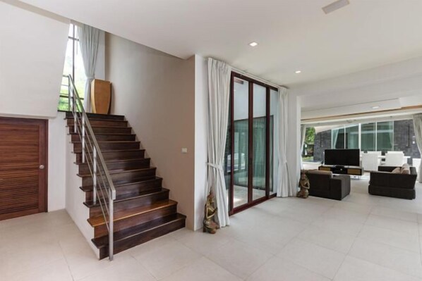 Una sala de estar moderna con una escalera, un puerta de vidrio y un televisor de pantalla plana.