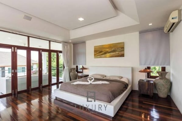 A spacious bedroom with a large bed, a painting on the wall, and a view through the glass doors. - Unique Pool Villa with 5 Bedrooms and Sea View (PM-C1) (Hua Hin)
