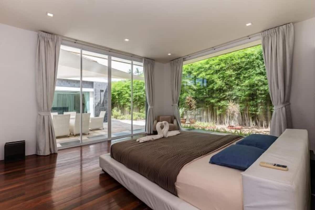 Une chambre moderne avec un grand lit, une vue sur la verdure et une porte-fenêtre coulissante donnant sur un espace extérieur.