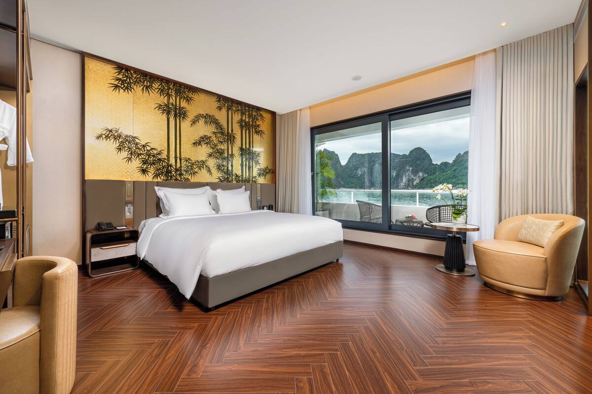 A modern hotel room with a large bed, a seating area, and a view of the sea.