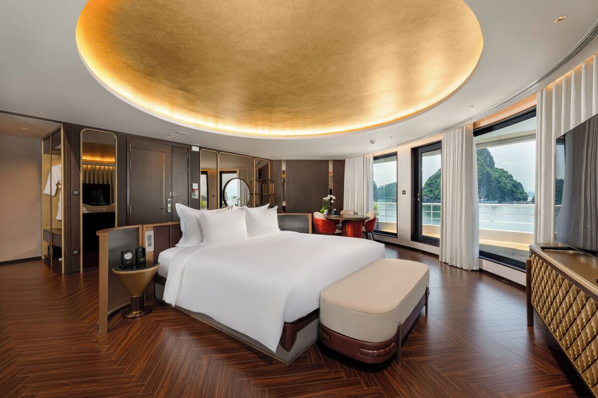 A modern hotel room with a large bed, a desk, and a view of the sea.