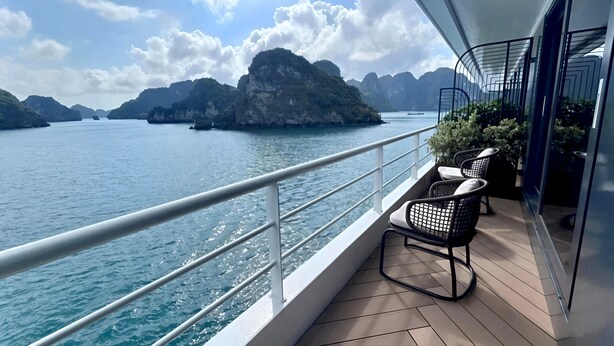Een balkon met uitzicht op zee en bergen, met twee rieten stoelen en een potplant.