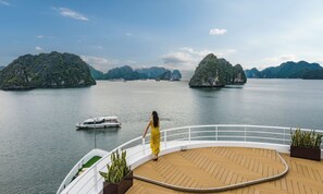 A woman in a yellow dress on a boat deck with a view of a calm sea and green islands. - Sea Stars Premium Cruises (Ha Long)