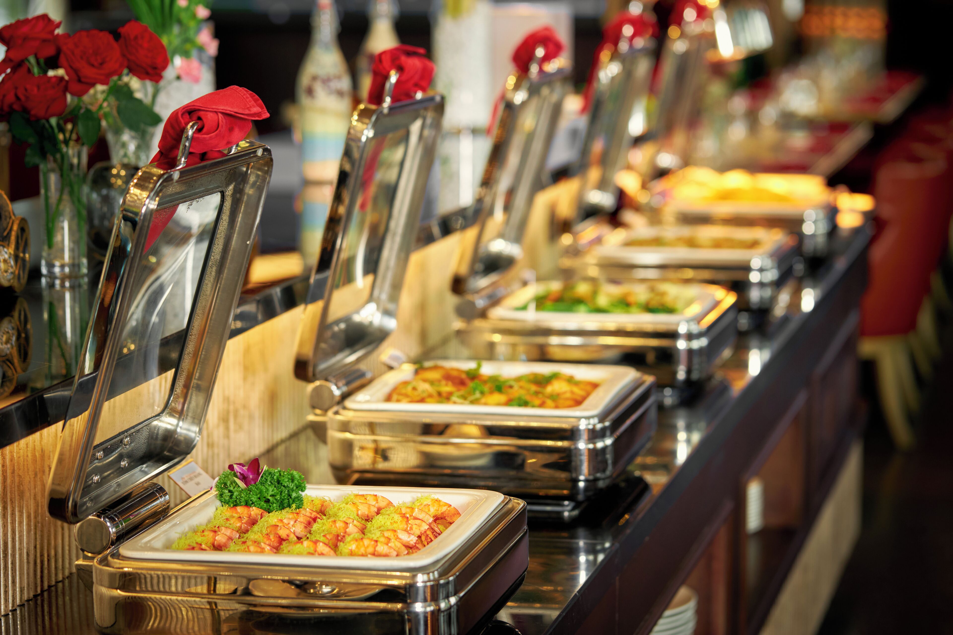 A buffet line with multiple serving stations, each with a metal tray and a red napkin on the chair.