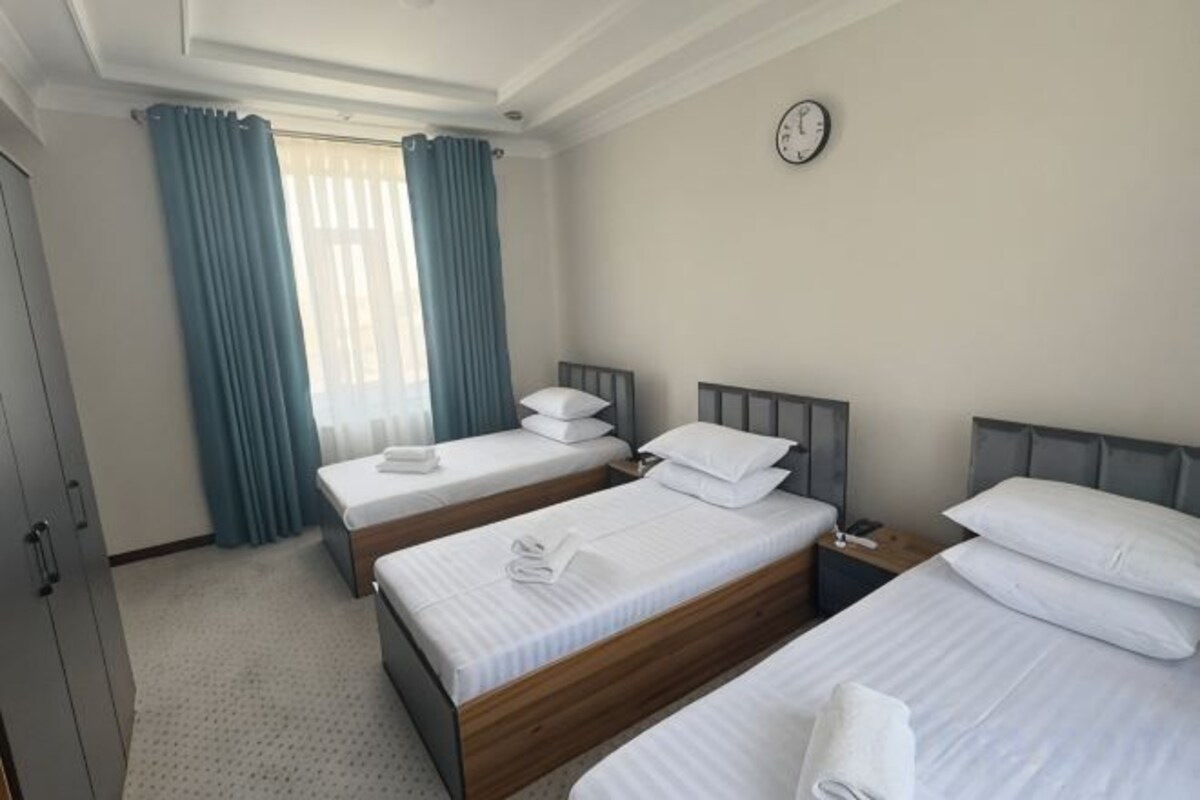 A hotel room with three beds, a wardrobe, and a clock on the wall.