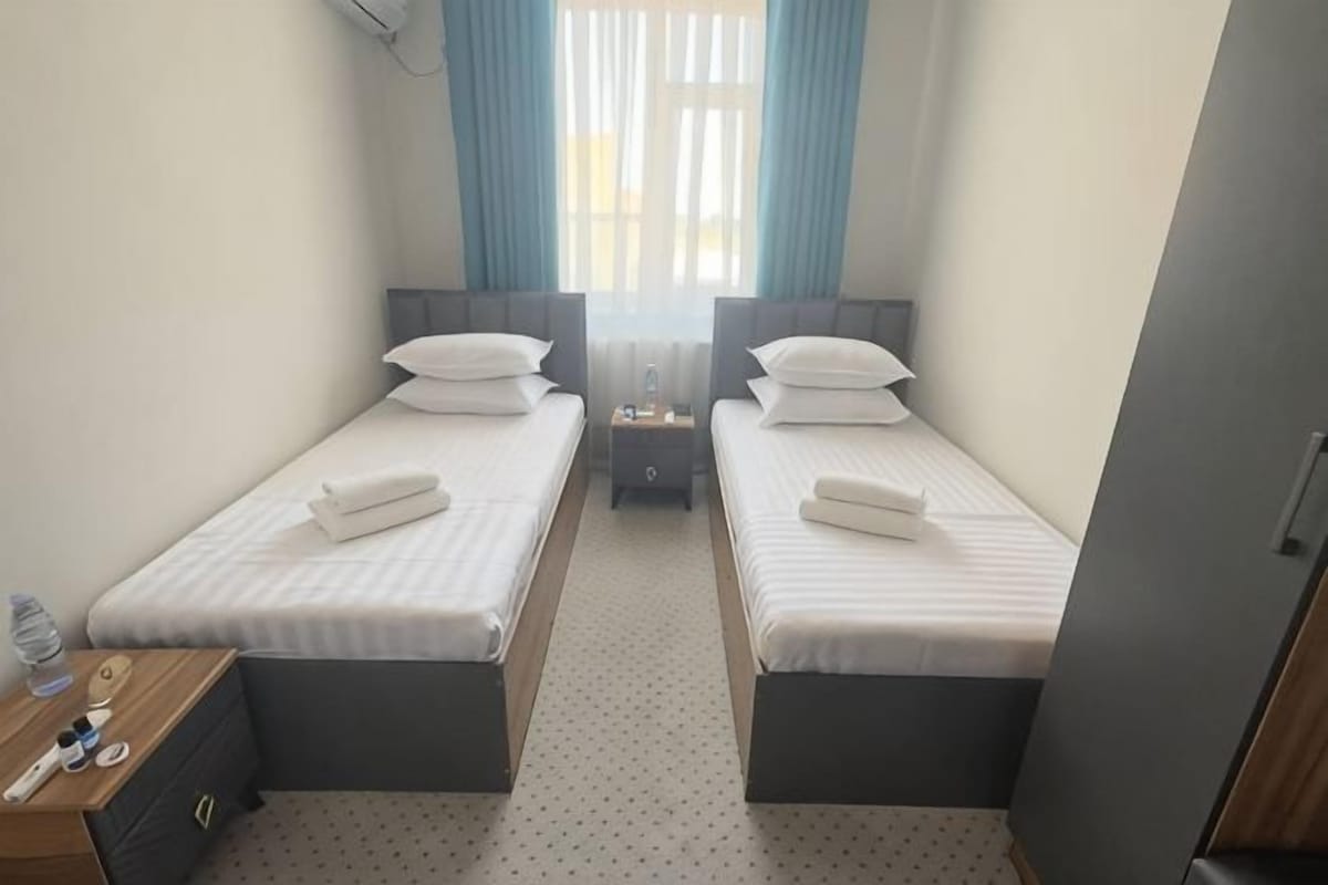 A twin room with two single beds, a small table with a lamp, and a wardrobe.