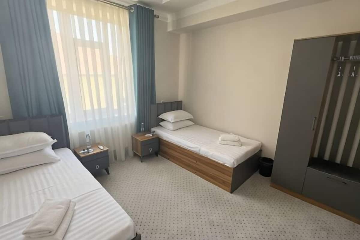 Habitación de hotel con dos camas, un armario, una mesita de noche y una ventana con cortinas.