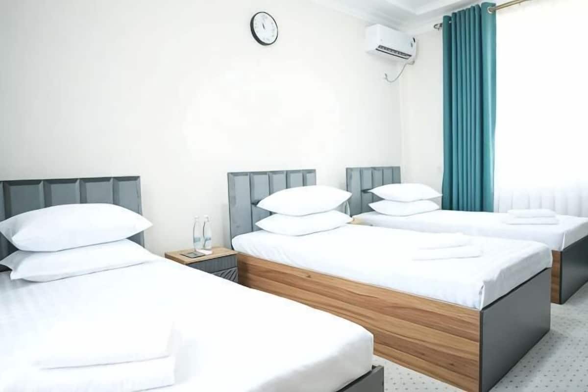 Habitación de hotel con tres camas, un reloj, aire acondicionado y una ventana con cortinas.