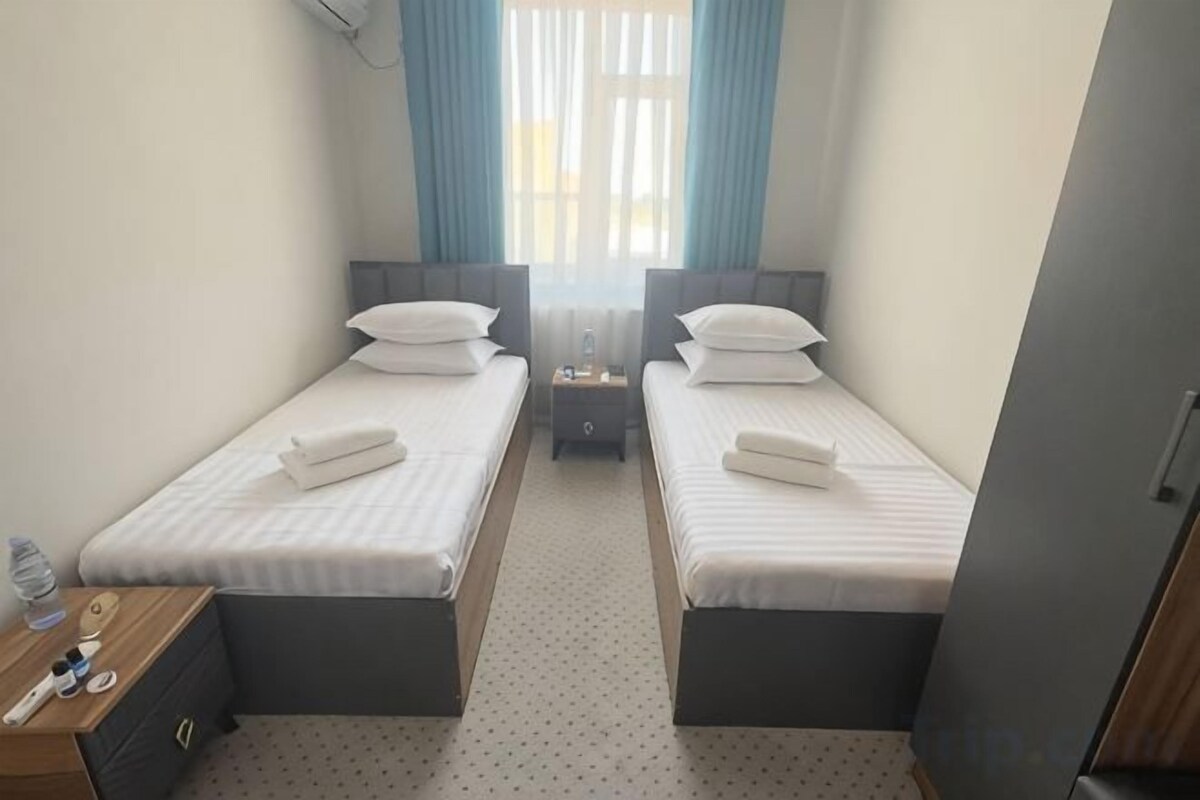 A twin bedroom with two single beds, a nightstand, a dresser, and a window with curtains.