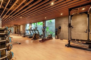 Un gimnasio con máquinas de cardio, equipo de levantamiento de pesas y piso de madera.