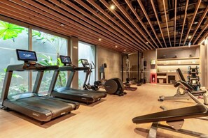 Une salle de sport équipée de tapis de course, d’appareils de musculation et dotée d’une grande fenêtre donnant sur un espace verdoyant.