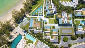 Luchtbeeld van een modern resort met meerdere zwembaden, weelderige beplanting en een strand.