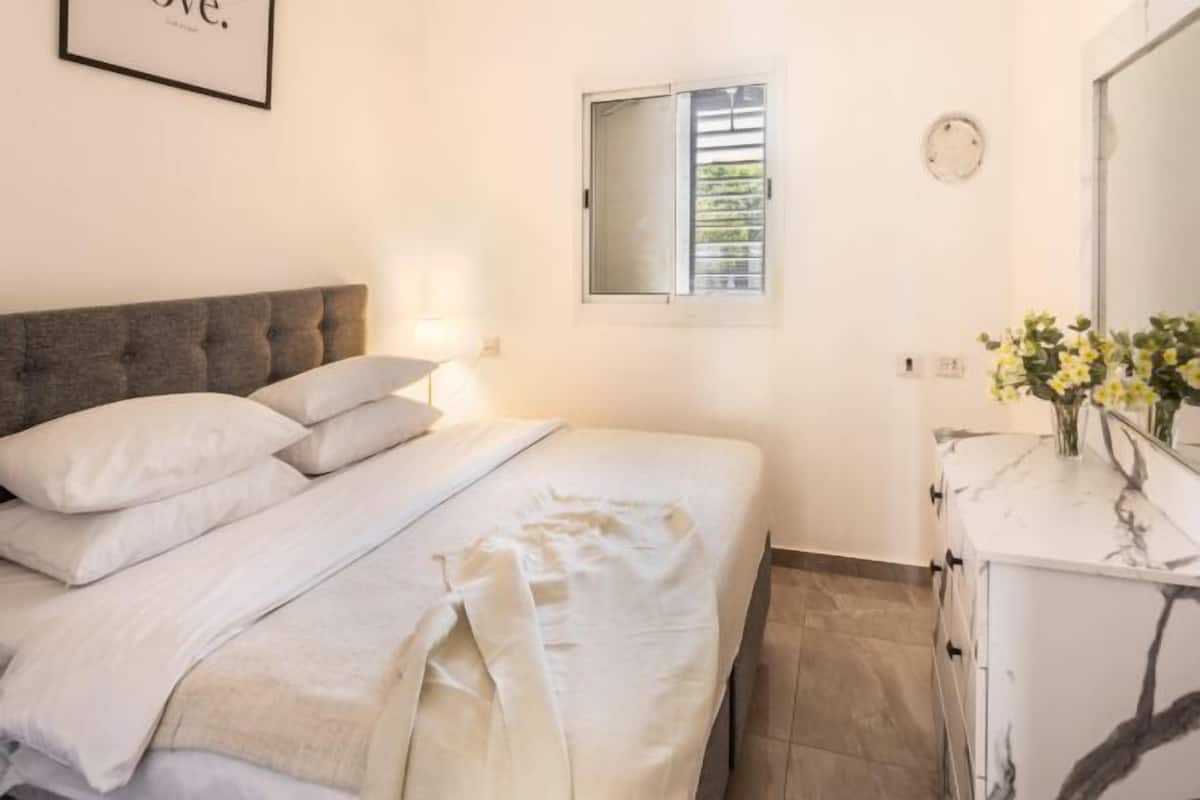 A bedroom with a bed, a dresser, a mirror, and a window.
