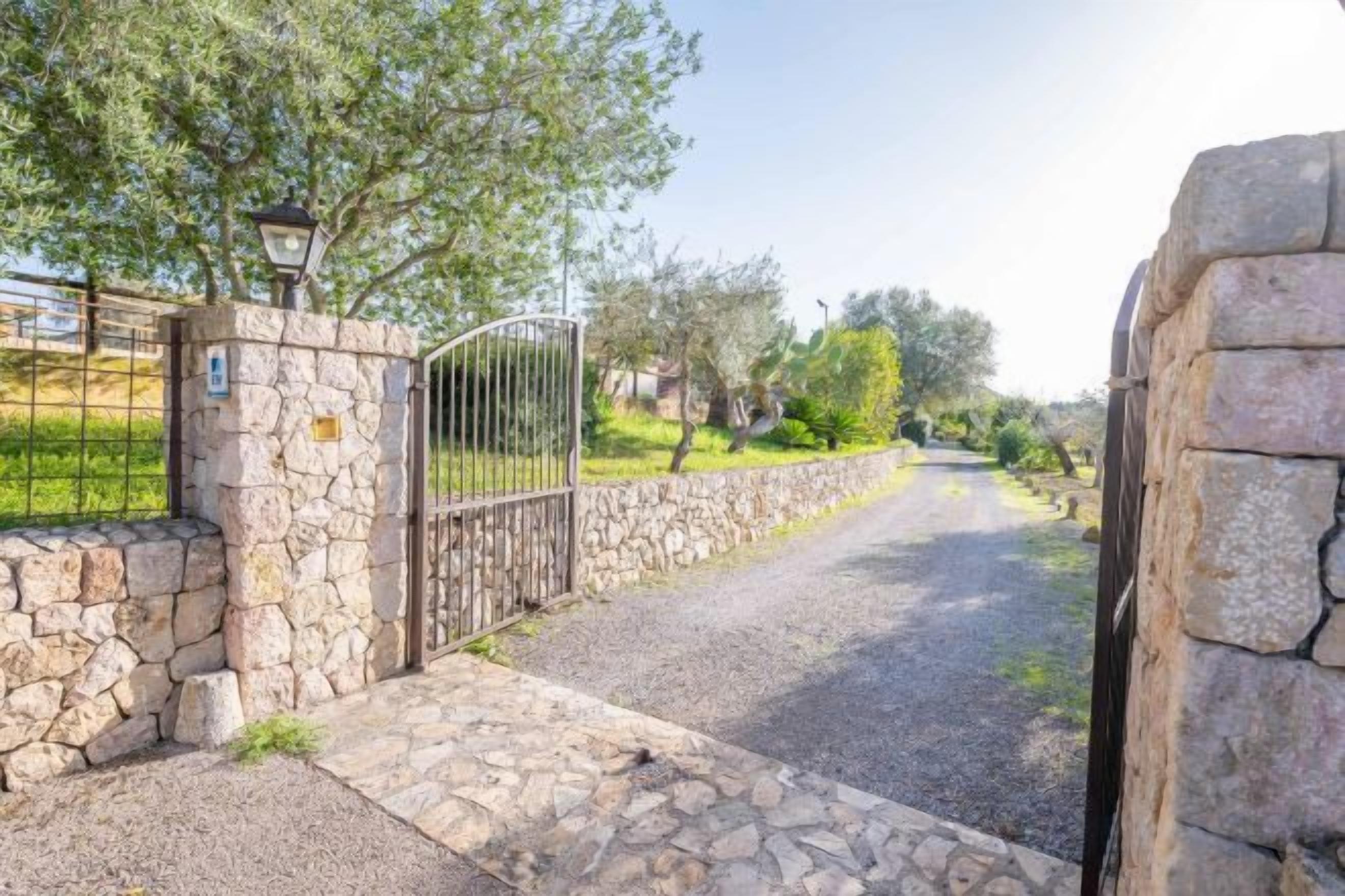 A paved pathway leading to a gated entrance with stone walls and a metal gate.