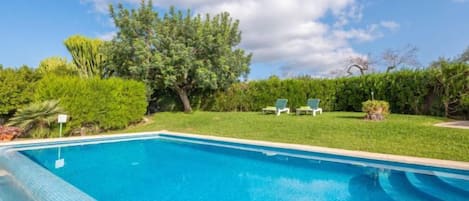 A swimming pool with a clear blue water surface, surrounded by a well-maintained lawn and trees.