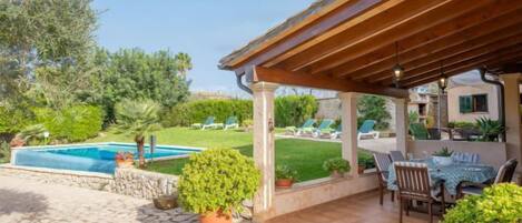 A covered outdoor area with a pool, stone flooring, and potted plants.