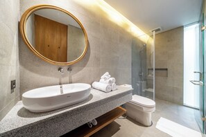 Ein modernes Badezimmer mit einem großen, ovalen Waschbecken, einem runden Spiegel, einer Toilette und einer Duschkabine aus Glas.