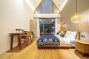 Ein Schlafzimmer mit einem großen Bett, einem Schreibtisch und einem Stuhl. Ein Fenster mit Vorhängen bietet Blick auf Bäume.