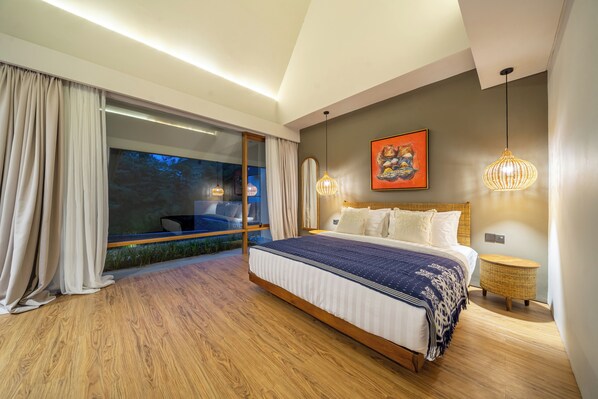 A modern bedroom with a large bed, a view through a glass door, and a painting on the wall. - Villa Manawa by Jawatra (Canggu)