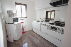 A compact kitchen with a microwave, stove, sink, and white cabinetry. - QiQi House Serenity~Private Near Asakusa & Skytree (Tokyo)