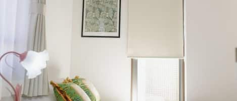 A bedroom with a bed, a window with curtains, a wall-mounted picture, and a bedside table with a lamp.