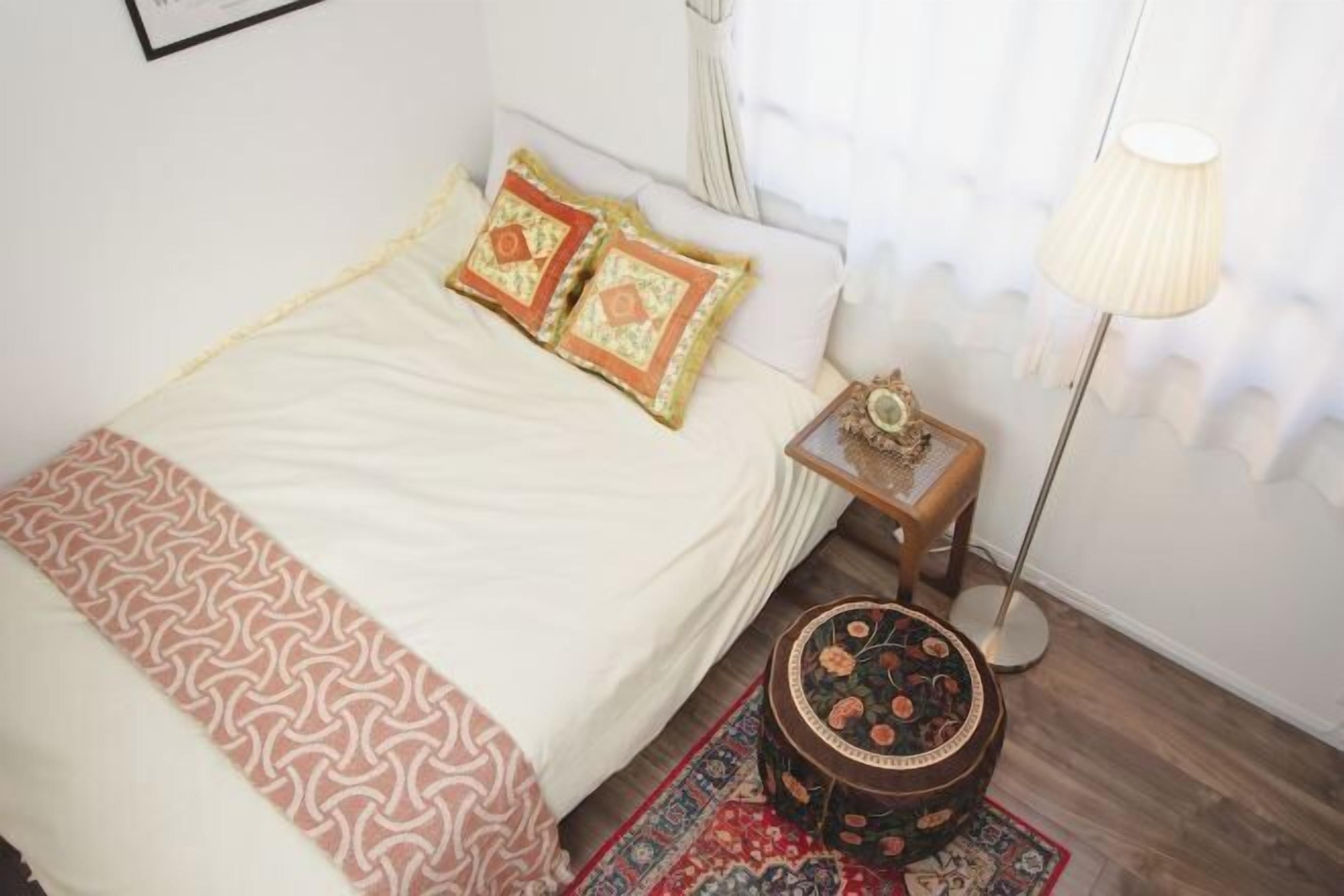 Un llit ben fet amb roba de llit estampada, una petita taula de nit amb una làmpada i una catifa decorativa.