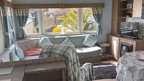 A compact living space with a sofa, a television, and a small kitchen area. - Spacious Holiday Home in Exmouth Ocean V (Exmouth)