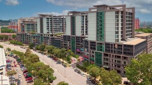 A modern multi-story building with a glass facade, surrounded by a parking lot and a street with cars. - Modern Comfy Bdr Permaisuri 2 parking WIFI Netflix (Kuala Lumpur)