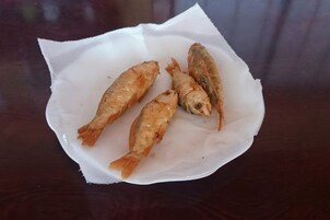 Three fried fish on a white paper on a wooden table.