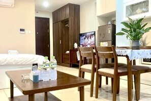 A hotel room with a bed, a dining table with chairs, a TV, a wardrobe, and a potted plant. - HaChu House (Hanoi)