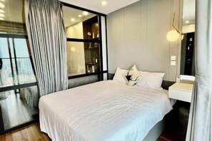 A modern hotel room with a large bed, a bedside table, a mirror, and a view through a window with curtains. - HaChu House (Hanoi)