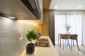 A modern kitchen with a built-in stove, a sink, and a dining area with two chairs and a table. - HaChu House (Hanoi)