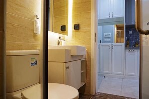 A bathroom with a toilet, sink, mirror, and cabinets. - HaChu House (Hanoi)