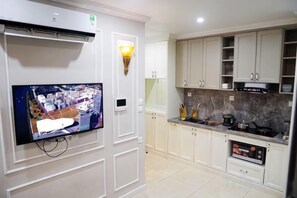 Una cuina moderna amb armaris blancs, un fogó encastrat i un televisor pantalla plana penjat a la paret.