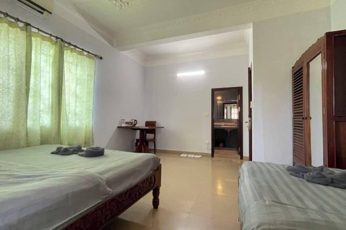 Ein Hotelzimmer mit zwei Betten, einem kleinen Tisch mit Stuhl und einer Tür zu einem anderen Raum.