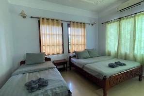 A bedroom with two beds, a nightstand, and a window with curtains.