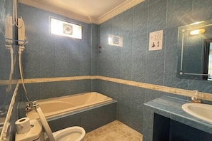 A bathroom with a bathtub, toilet, and sink, featuring dark blue tiles and a wooden accent strip.