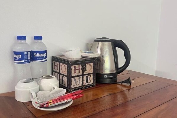 A wooden table with a black cube labeled "HO HO HO," two water bottles, a white teapot, a silver electric kettle, and a pair of scissors.