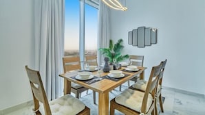 Un espace repas comprenant une table en bois, des chaises, un luminaire suspendu moderne et une vue dégagée grâce à de grandes fenêtres.