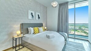 Une chambre d’hôtel moderne avec un grand lit, une table de chevet, une lampe, une vue sur la ville et des œuvres d’art accrochées au mur.