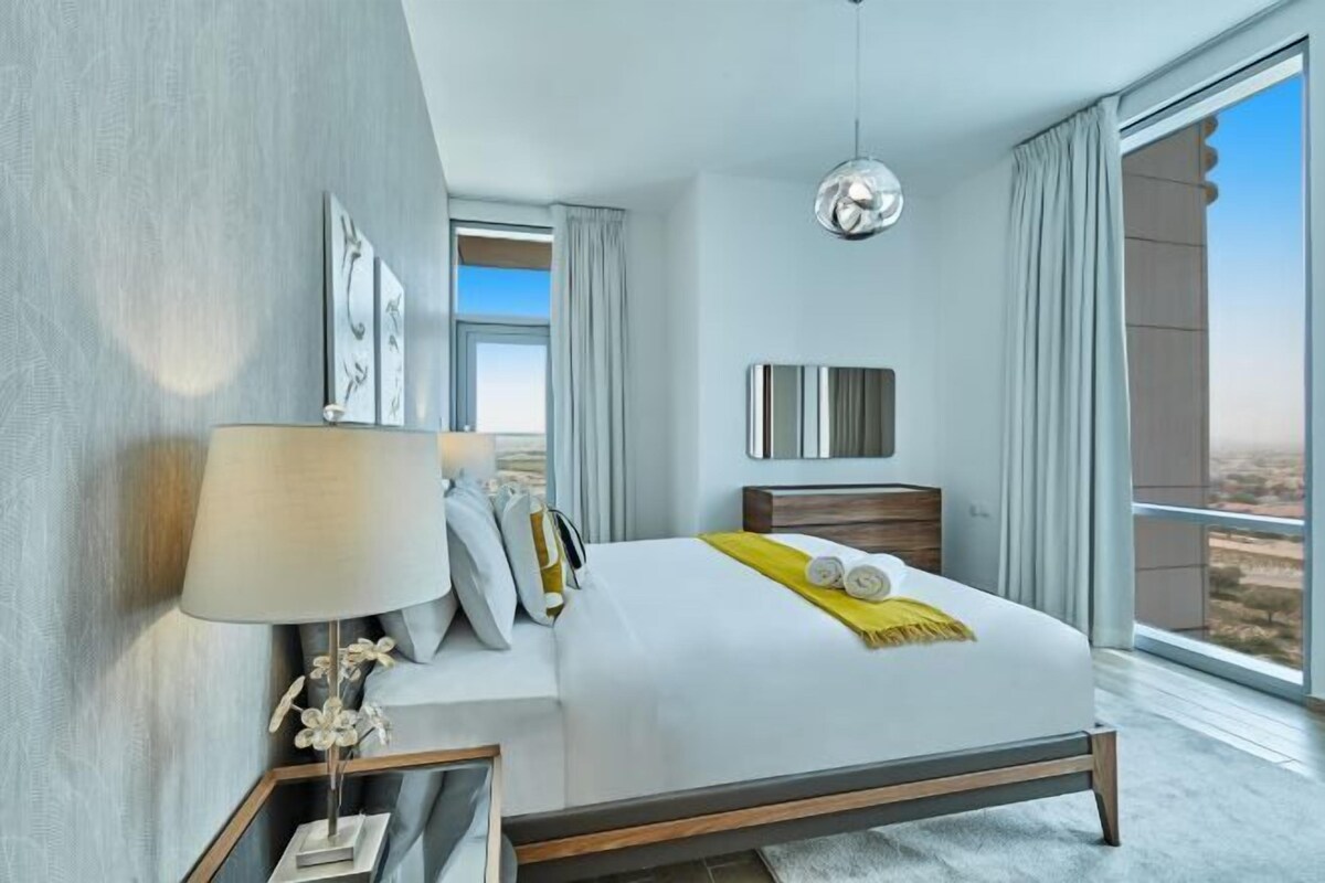Una habitación de hotel moderna con una cama grande, una mesita de noche con lámpara, vistas por la ventana y una lámpara colgante.