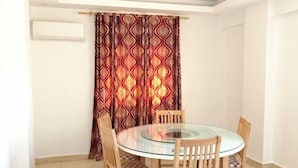 Un coin repas avec une table ronde en verre et des chaises en bois, un rideau à motifs et un appareil de climatisation fixé au mur.