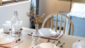 A dining table set with white plates, bowls, and cutlery, a clear glass bottle, and a vase with dried flowers. - Pinnacle Duplex@5m Walk to Paradigm Mall+WIFI (Petaling Jaya)