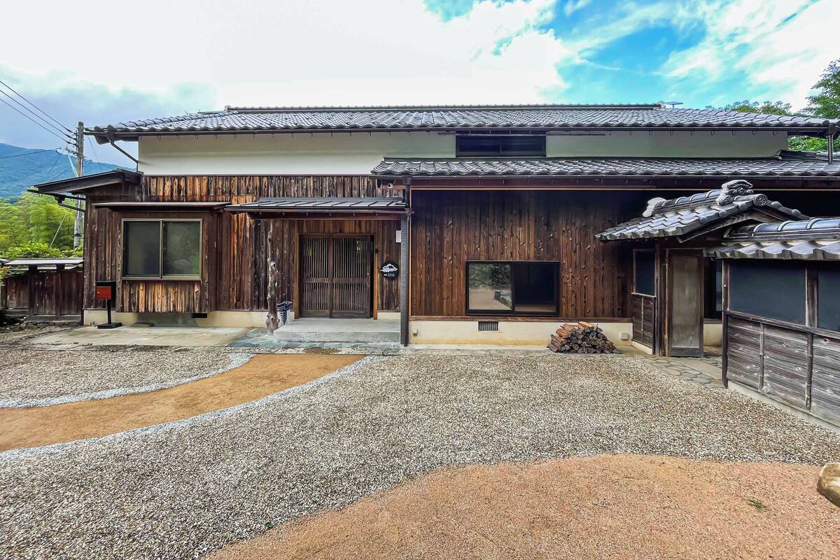 A traditional Japanese house with a wooden exterior, a tiled roof, and a gravel driveway.