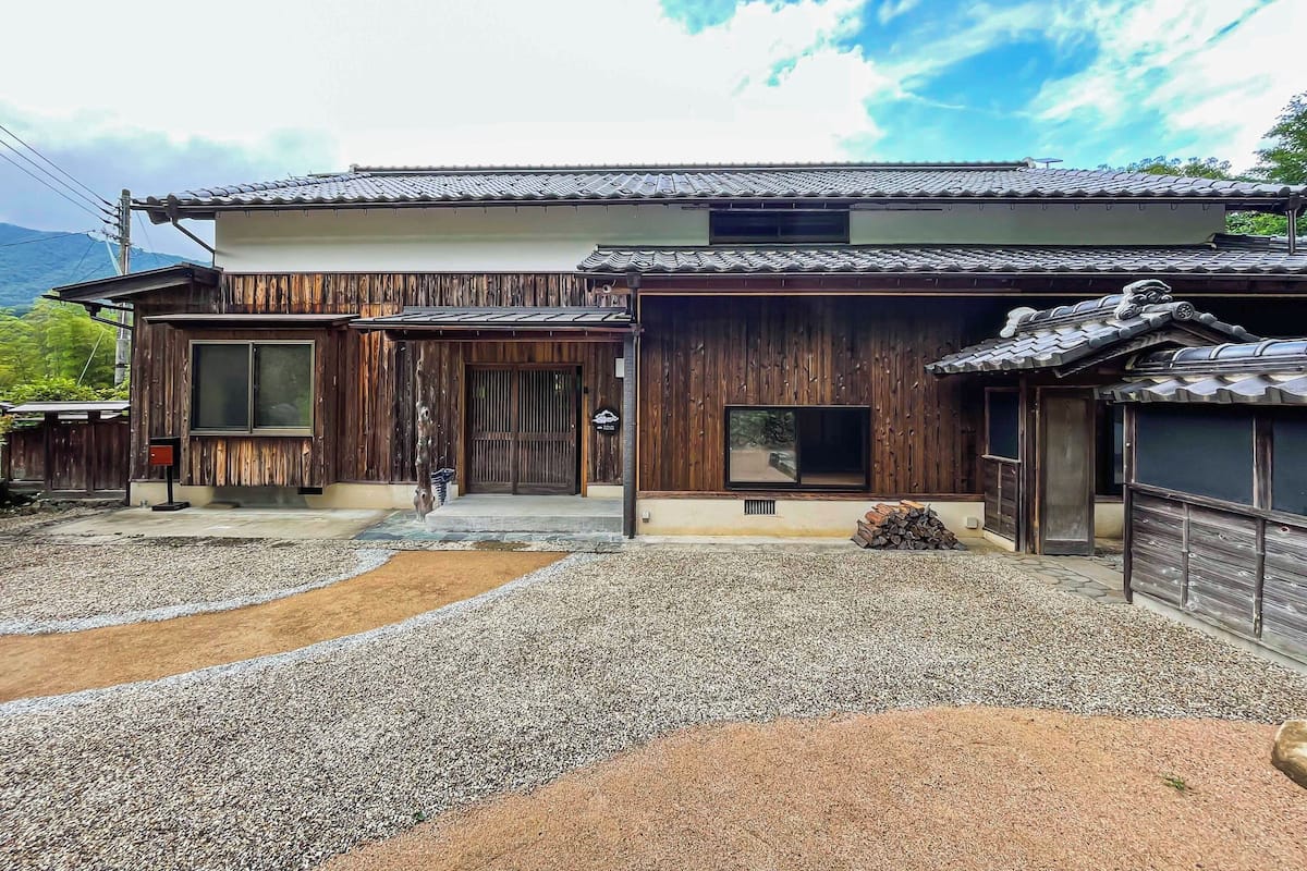 A traditional Japanese house with a wooden exterior, a tiled roof, and a gravel driveway.