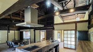 A spacious kitchen with a large island, wooden beams, and a high ceiling. - Takeda Base Inn (Asago)