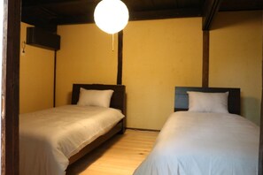Una habitación con dos camas, vigas de madera, un colgador de techo y una pared lisa.